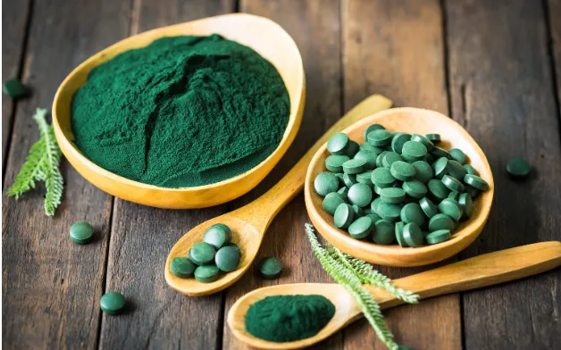 Ground and pilled spirulina in spoons and bowls, set over wood table