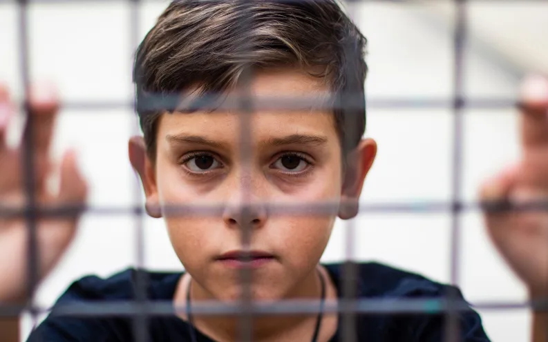 Young boy standing behind fenced wall, gripping with hands