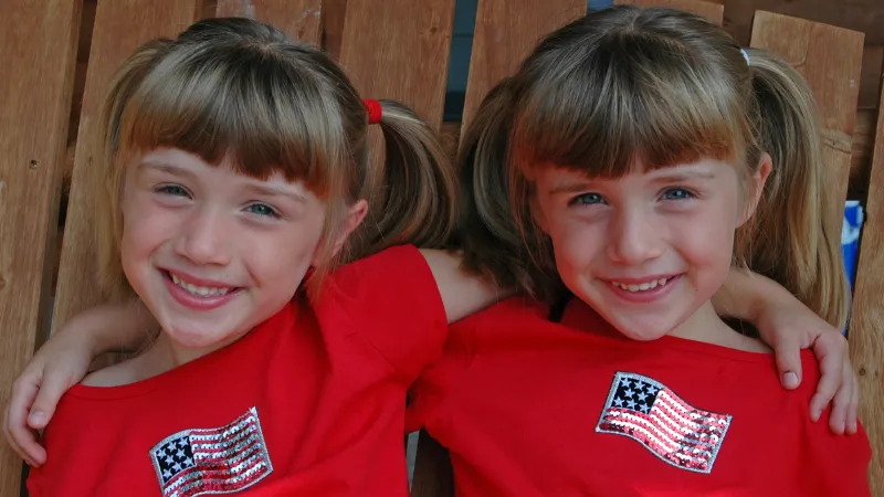 Twin girls arm-in-arm wearing red shirts with American flag emblazoned on them