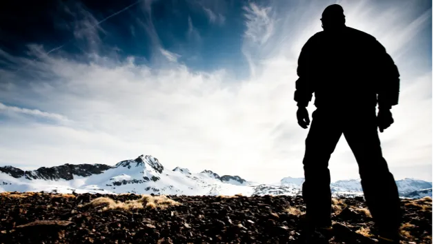 Man standing strong, in silhouette, facing mountain