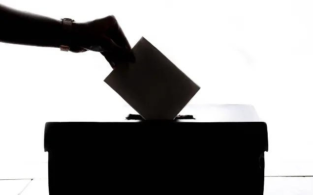 Black and white image of hand dropping ballot in box