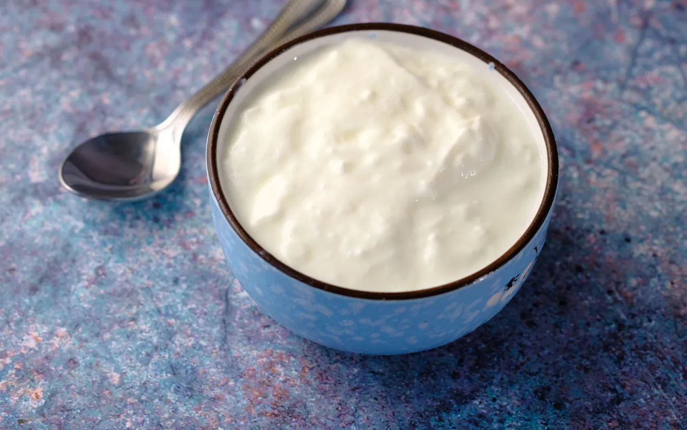 Bowl of fresh yogurt with spoon beside it, on table