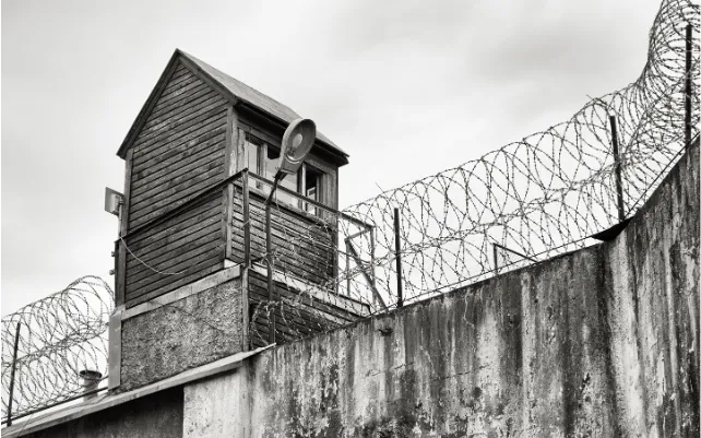 Guard tower over barbed wire-topped prison wall