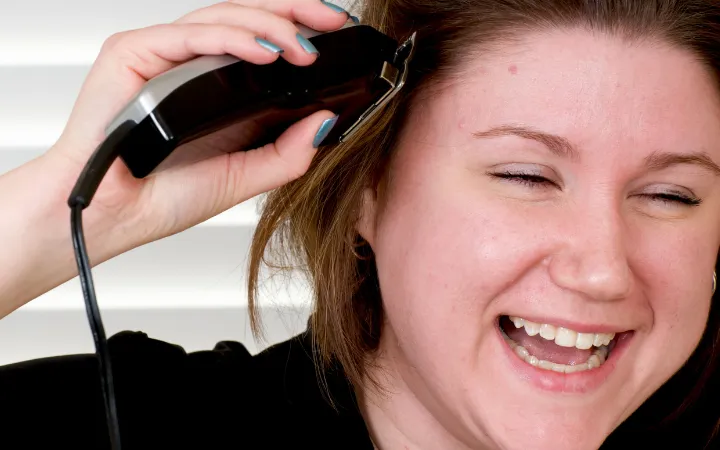 Woman shaving her head with electric clippers