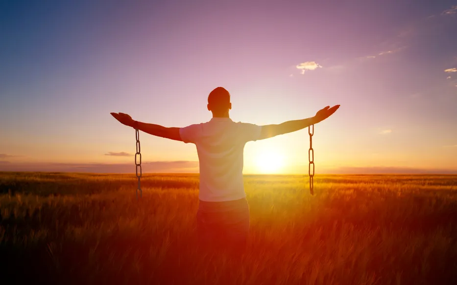 Man with broken chains, standing in field, facing a new dawn
